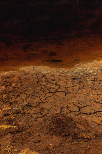 Detailed ground texture of dry cracked red soil, evoking elemental harshness