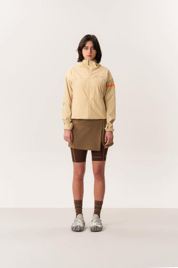 Model wearing beige packable rain jacket for hiking with light brown hardshell skirt in studio lighting