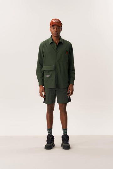 Model wearing dark green overshirt and green wrinkled shorts in clean studio environment
