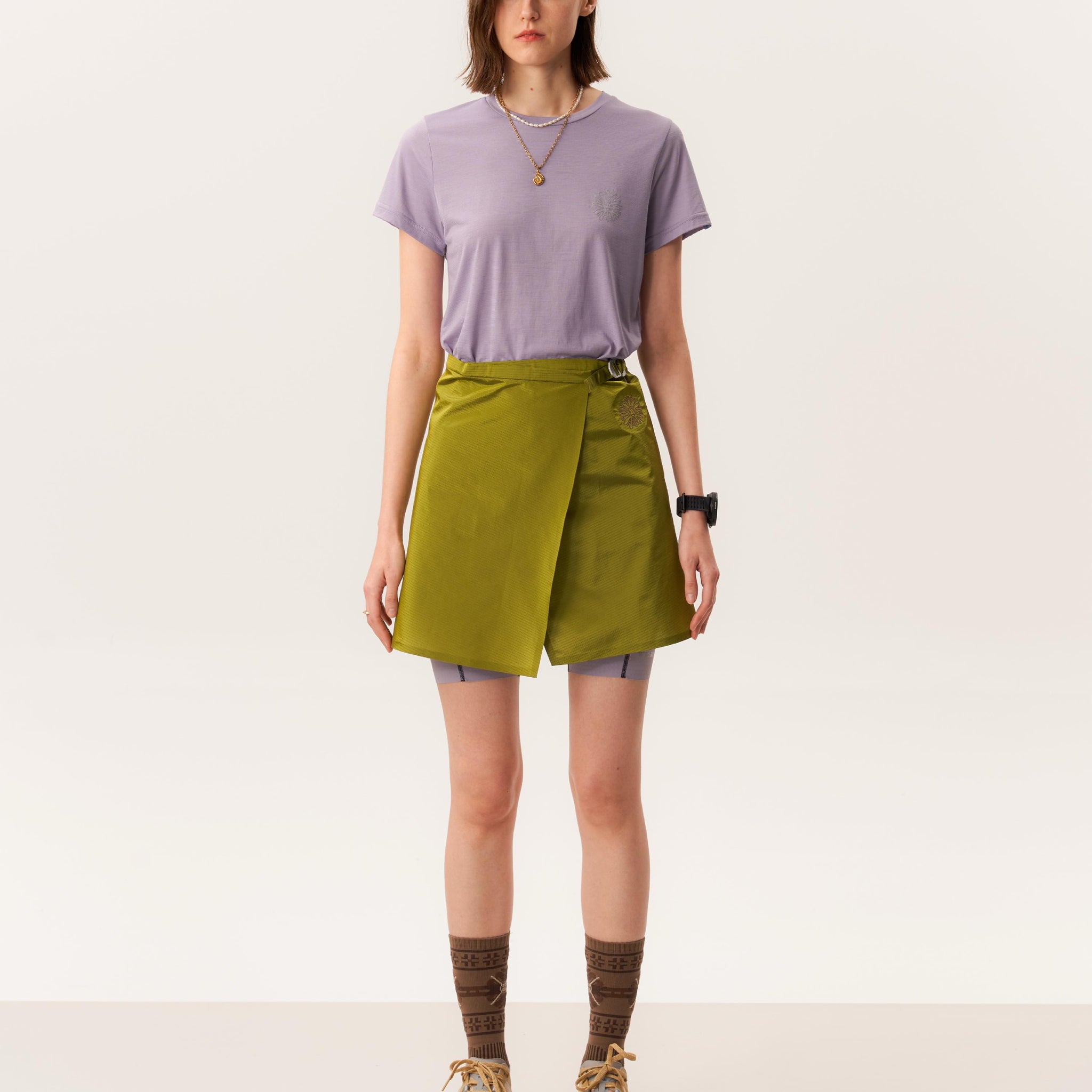 Studio shot of model wearing green short mini skirt and merino wool base layer T-shirt