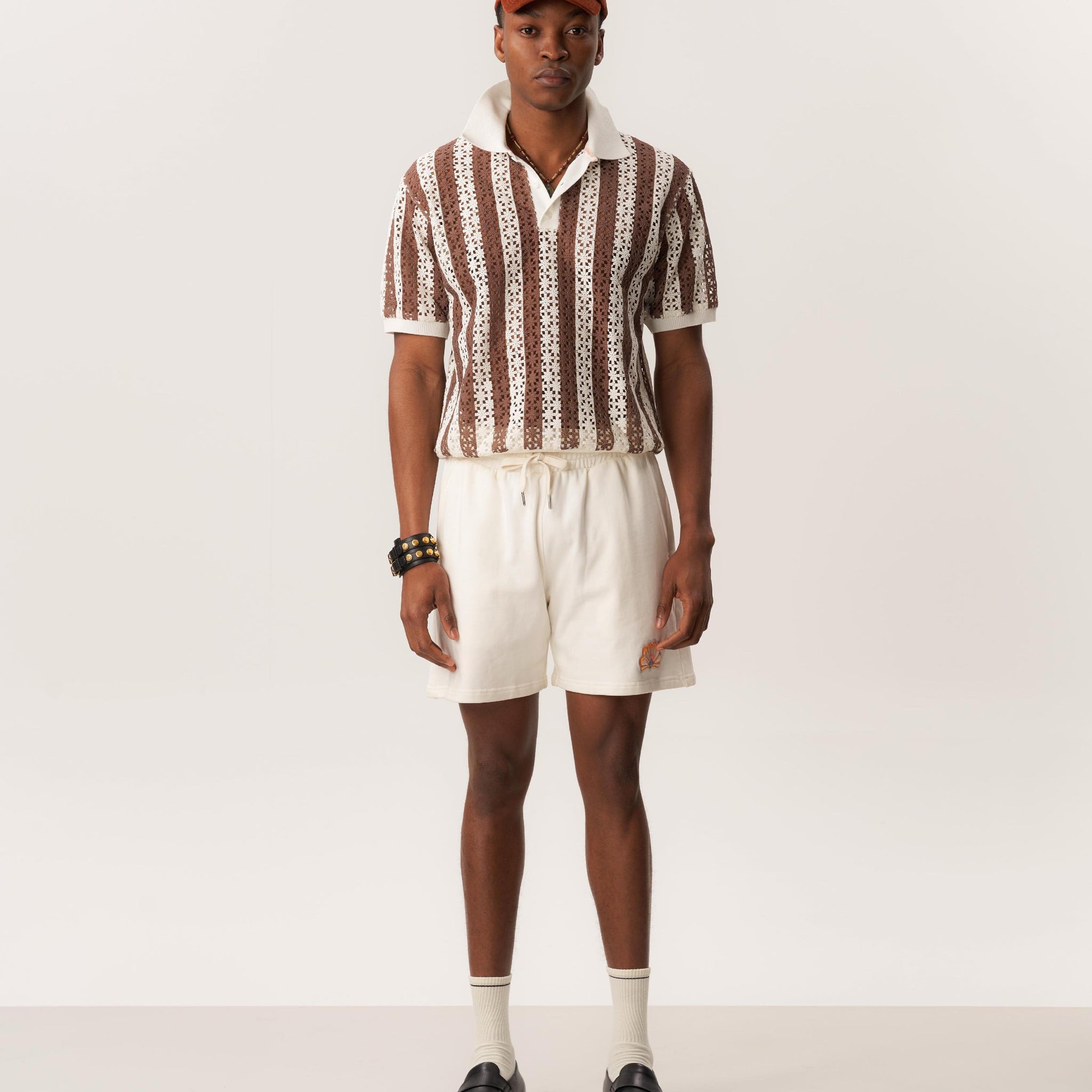 Model wearing openwork knit polo shirt and white shorts in relaxed studio setting