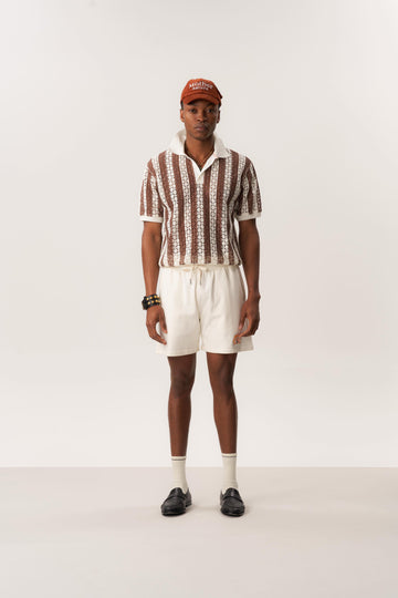 Model wearing openwork knit polo shirt and white shorts in relaxed studio setting