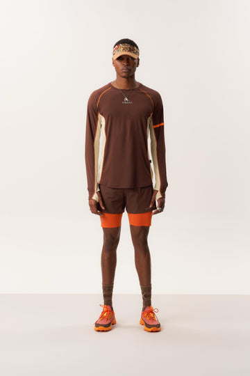 Model wearing SACI long sleeve moisture wicking shirt and ENSIGN S 5-inch trail shorts with built-in liner on studio backdrop