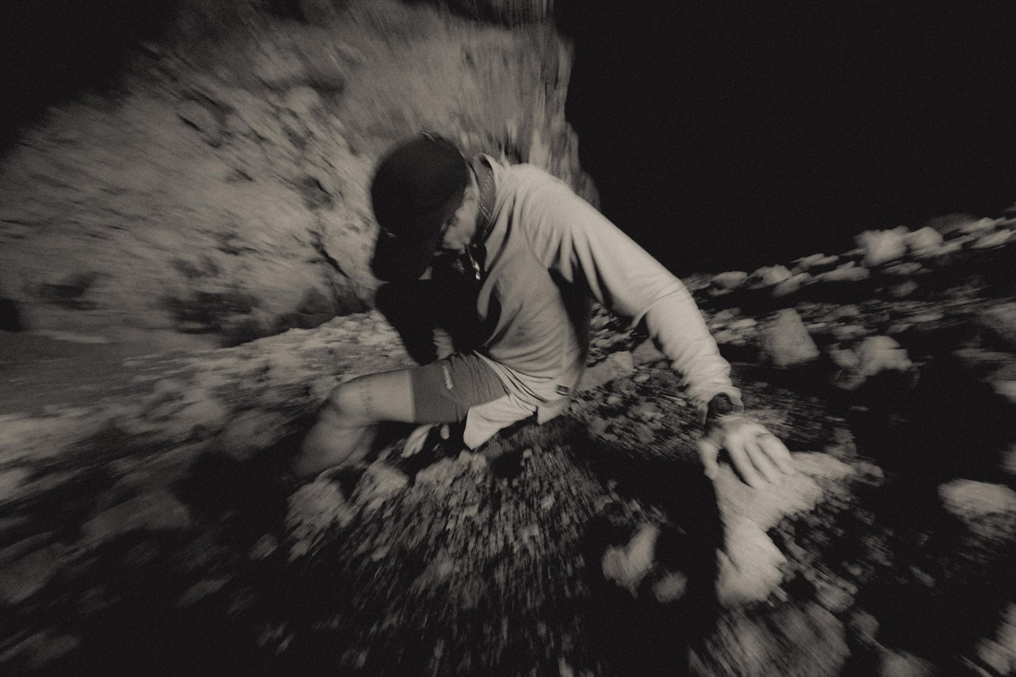 Black-and-white blurred photo of model crawling or climbing over rough terrain, intense movement