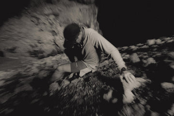Black-and-white blurred photo of model crawling or climbing over rough terrain, intense movement