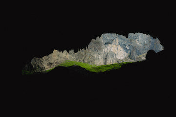Cave framing rugged stone mountains and vibrant grasslands under midsummer light